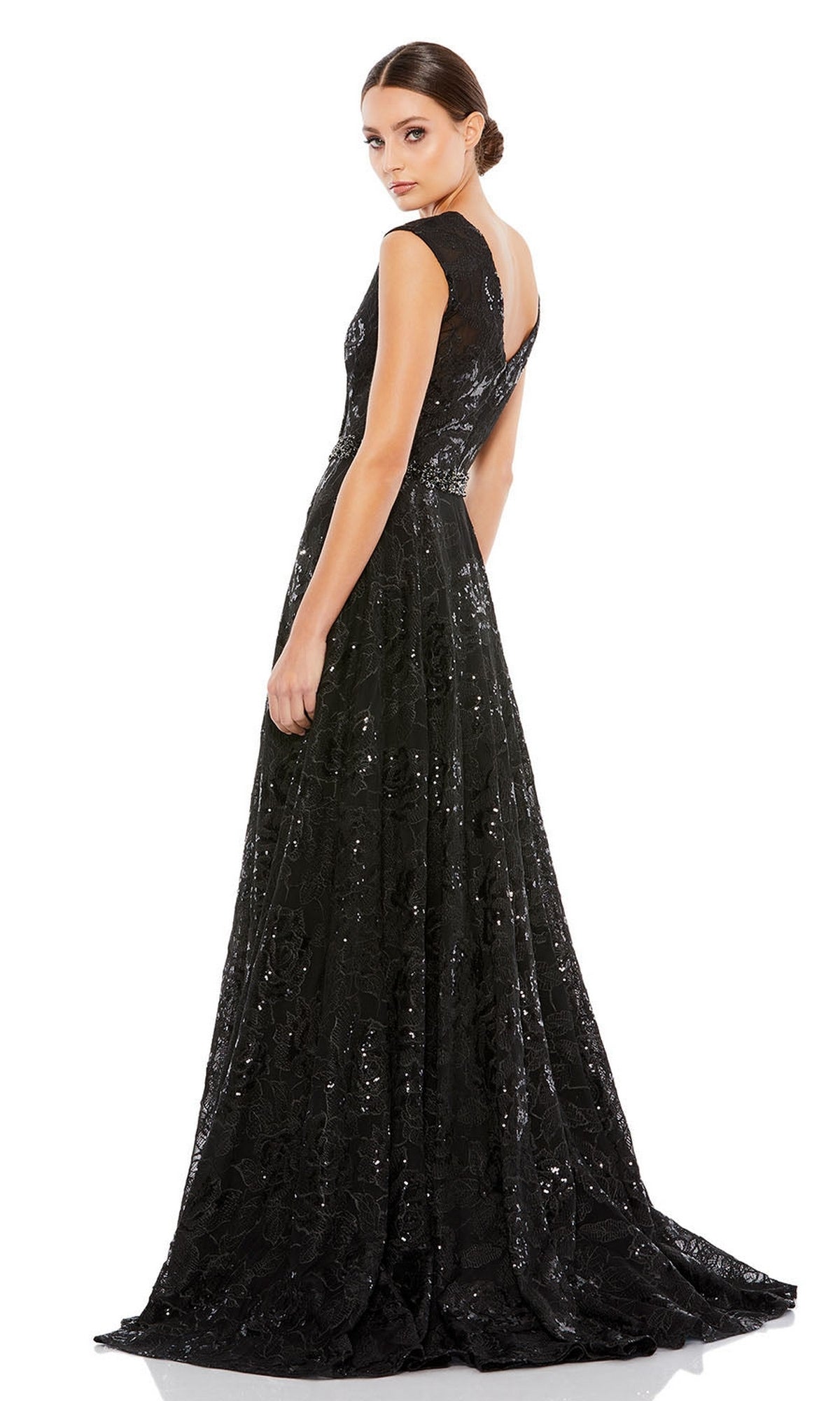 A woman models the Long Formal Dress 12413 by Mac Duggal, a floor-length black embroidered gown, standing with her back slightly turned and looking over her shoulder against a white background.